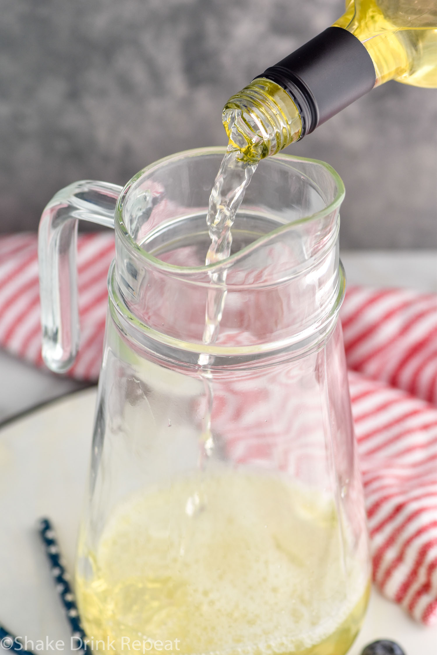 Side view of bottle of white wine being poured into pitcher for Fourth of July Sangria recipe