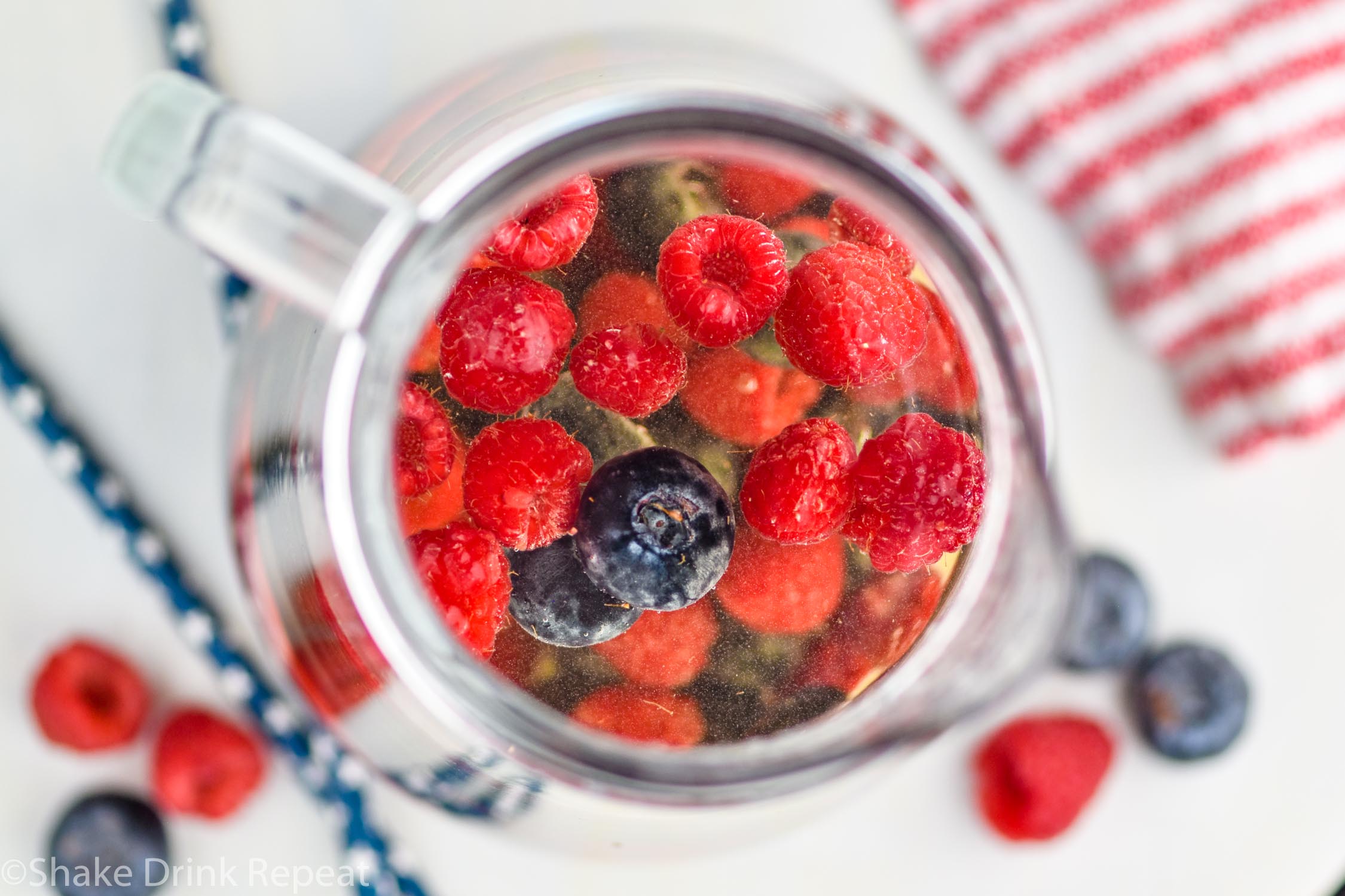 Overhead photo of a pitcher of Fourth of July Sangria. Extra raspberries and blueberries beside pitcher on counter.