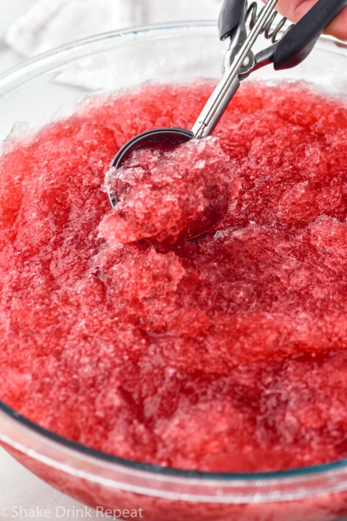 Overhead view of a cookie scoop scooping out Frozen Cosmos from a large bowl of Frozen Cosmos recipe.