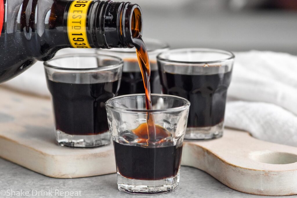 Side view of Kahlua being poured into shot glasses for Baby Guinness Shot recipe.