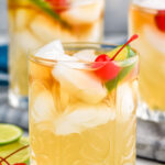 Side view of Mai Tai cocktail garnished with lime wedge and cherry. More glasses of Mai Tai in the background. Lime wedges and cherries beside the glasses for garnish.