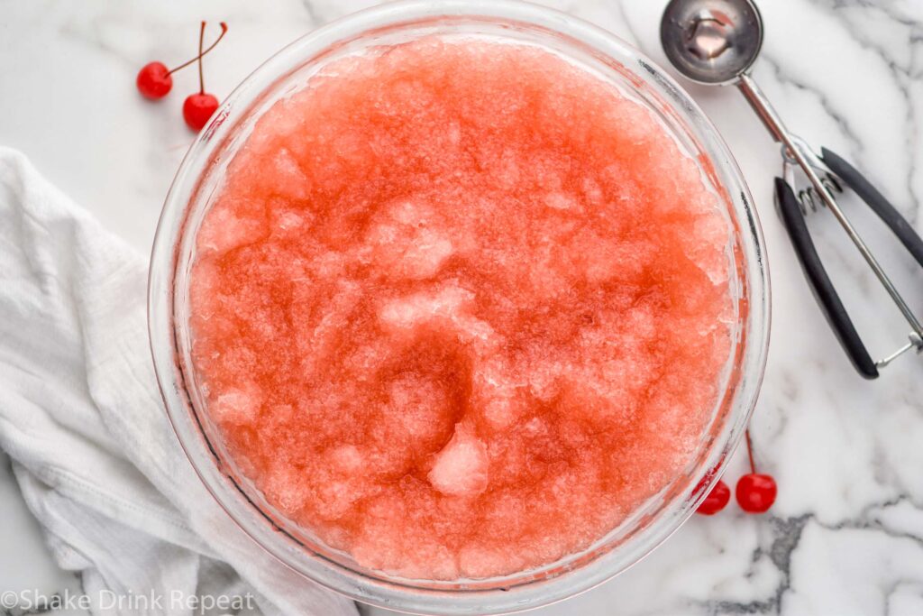 Overhead photo of a bowl of Dirty Shirley Slush. Cookie scoop and cherries for garnish beside bowl.