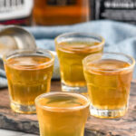 four shot glasses of three wise men shot. Bottles of whiskey sitting in background