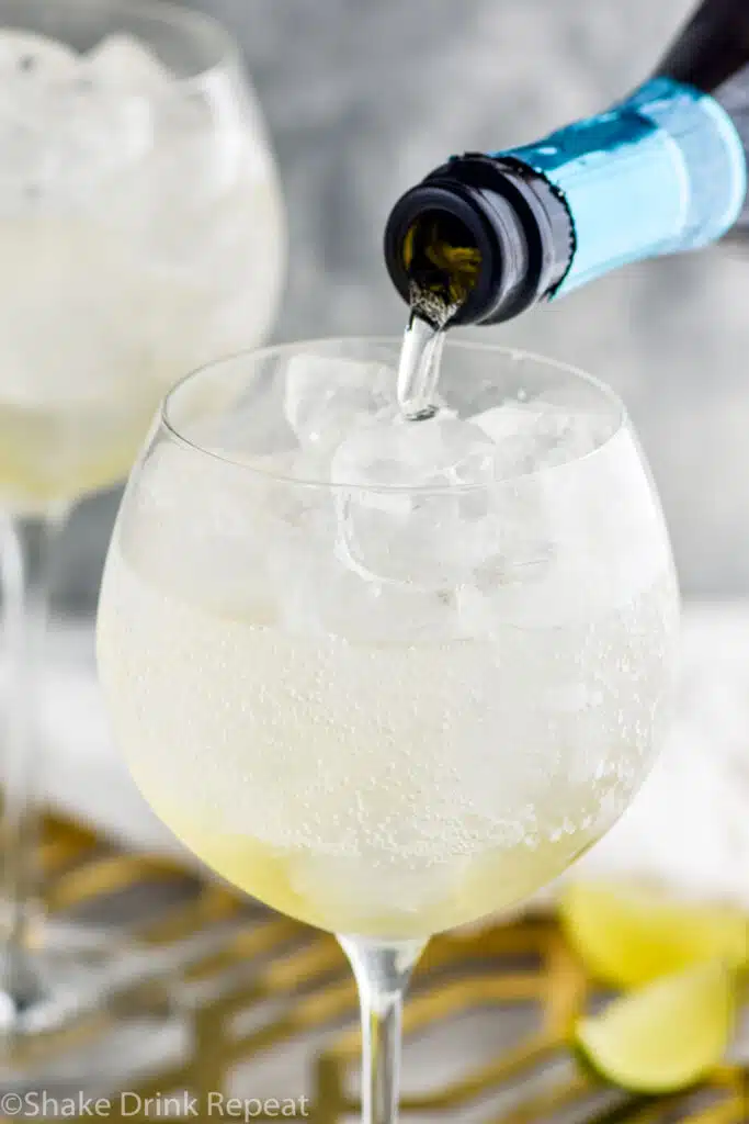 bottle of sparkling wine pouring into a wine glass of hugo spritz ingredients