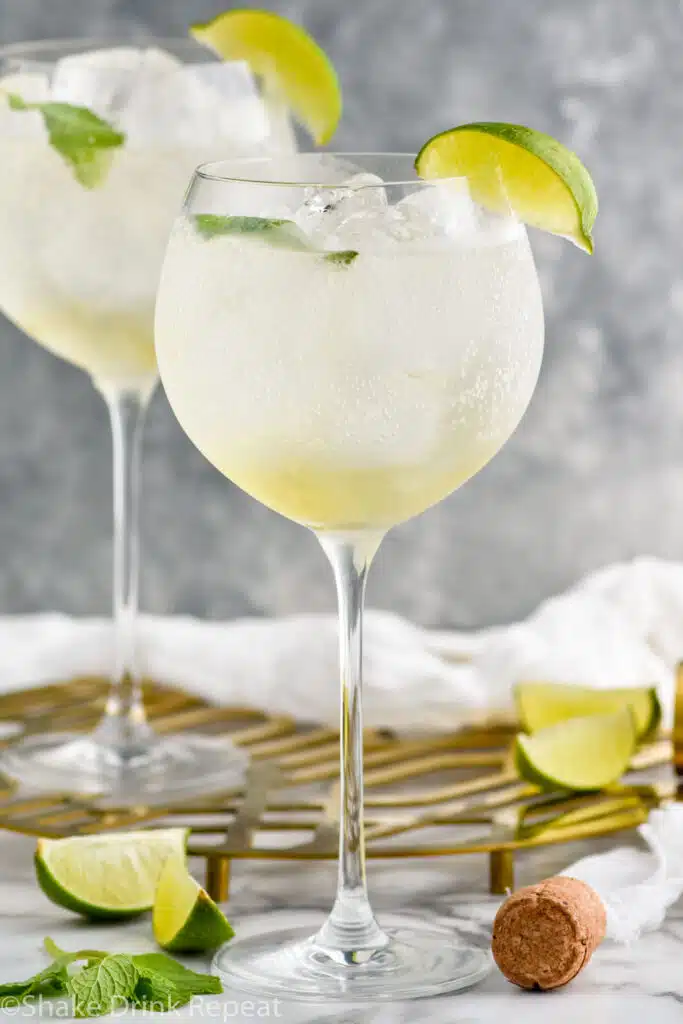 two wine glasses of Hugo spritz garnished with lime wedge and mint leaves