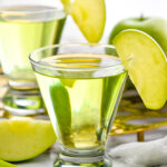 Two glasses of appletini cocktails garnished with an apple slice