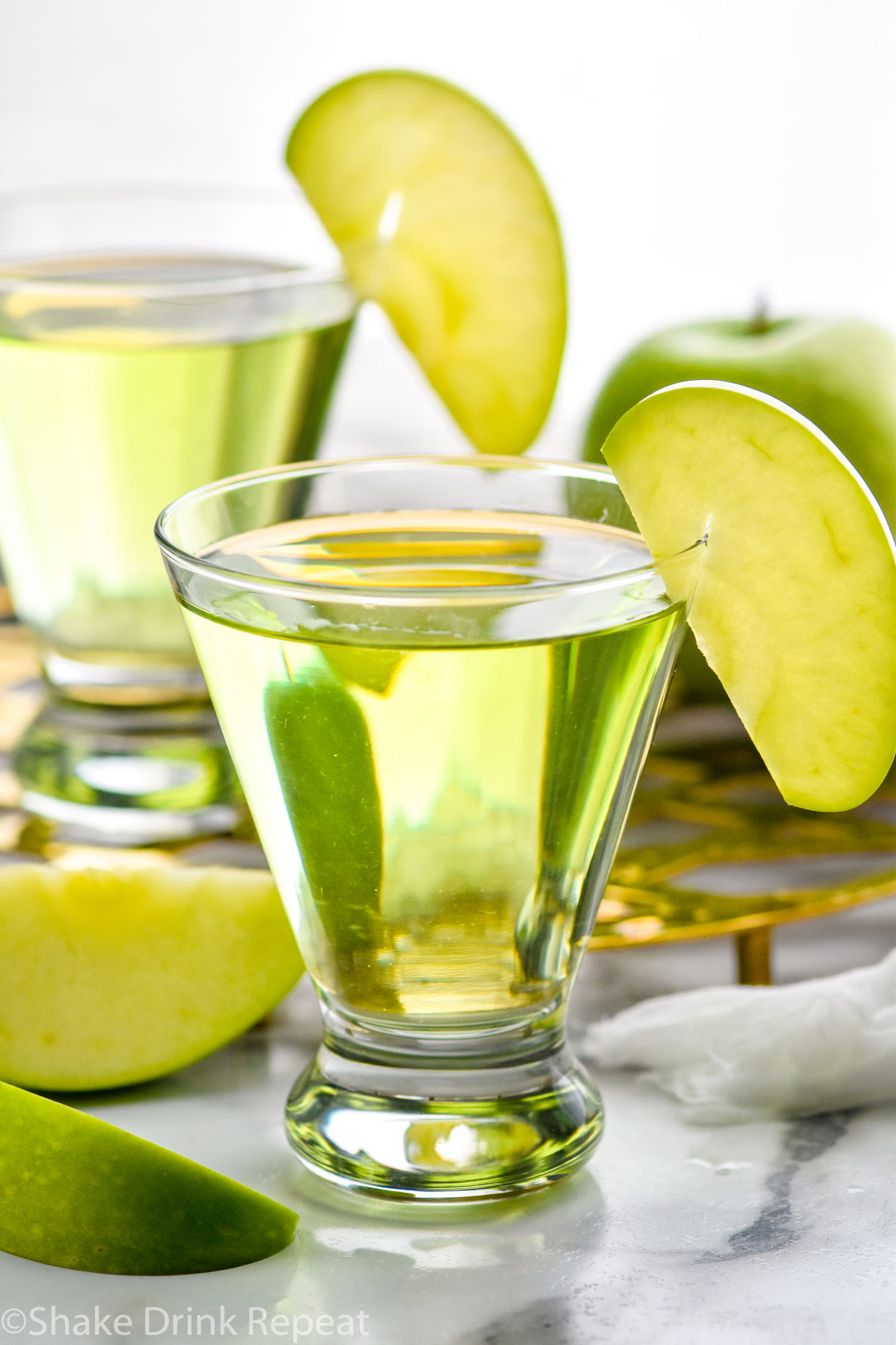 Two glasses of appletini cocktails garnished with an apple slice