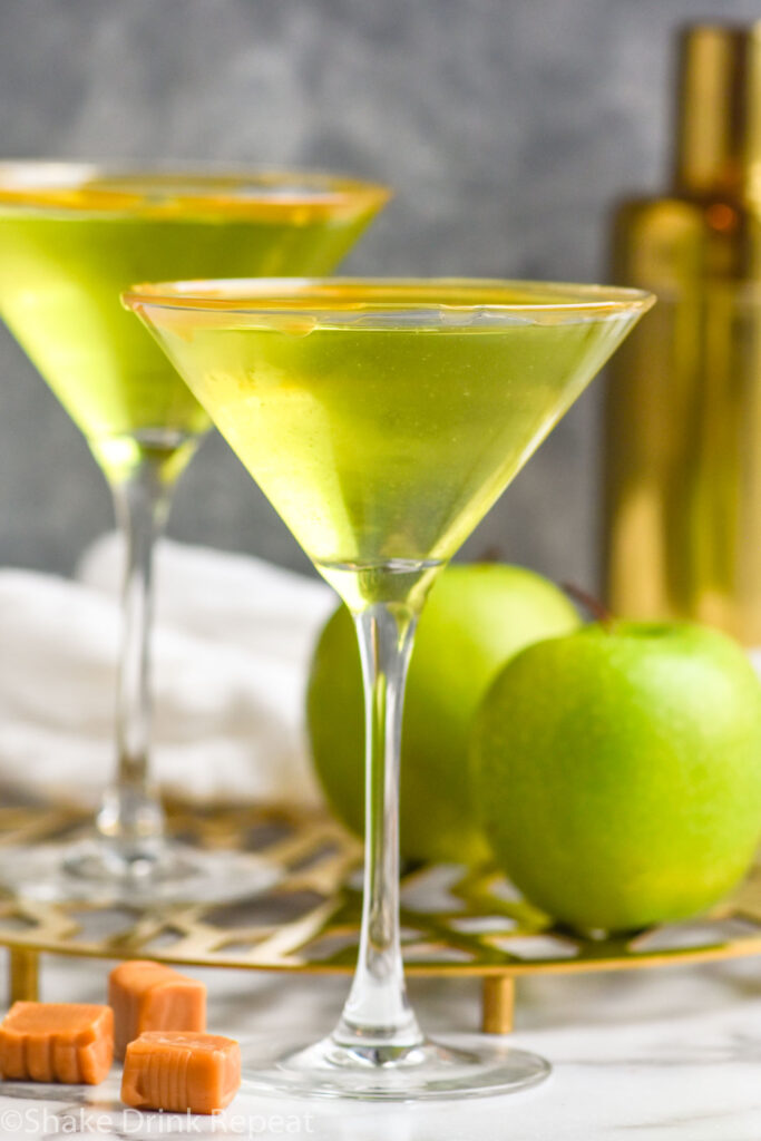 Side view of Caramel Apple Martinis with apples and caramel candies beside