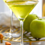 Side view of Caramel Apple Martini with apples and caramel beside