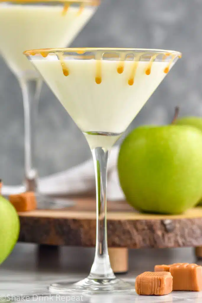 Side view of Creamy Caramel Apple Martini with apples and caramel candies beside
