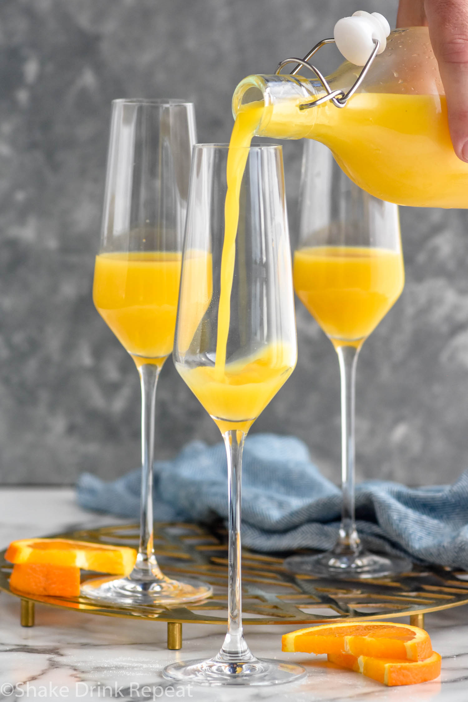 Side view of orange juice being poured into champagne flutes for Non Alcoholic Mimosa recipe. Orange slices beside.