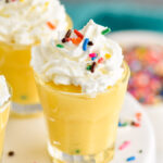 Birthday Cake Pudding Shots with whipped cream and sprinkles on a cake stand