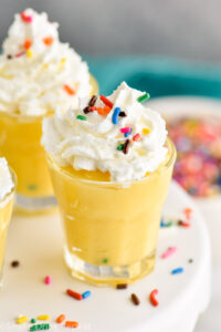 Birthday Cake Pudding Shots with whipped cream and sprinkles on a cake stand