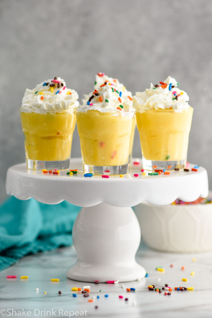 Birthday Cake Pudding shots on a cake stand surrounded by sprinkles