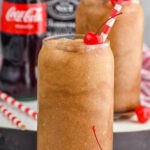 Frozen Jack and Coke drinks with straw and cherry. Bottle of coca cola and jack daniels beside.