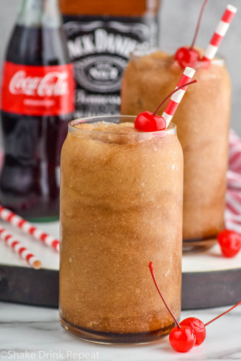 Frozen Jack and Coke drinks with straw and cherry. Bottle of coca cola and jack daniels beside.
