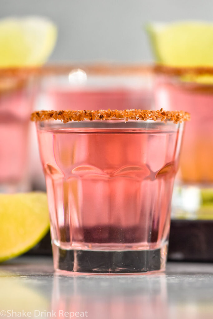 Side view of a Mexican Candy Shot with garnished rim. More Mexican Candy Shots and lime wedges beside.