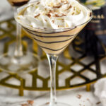 Baileys Martini topped with whipped cream, martini and bottle of baileys irish cream sitting in background.