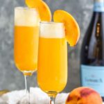 Pinterest graphic for Bellini. Text says "the best bellini only uses 2 simple ingredients! shakedrinkrepeat.com" Image shows two glasses of Bellini garnished with a slice of fresh peach. Peach and bottle of champagne sitting in background