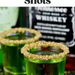 Pinterest graphic for lucky leprechaun shots. Text says "the best lucky leprechaun shots shakedrinkrepeat.com" The images shows two shot glasses of lucky leprechaun shots with bottle of whisky in the background.