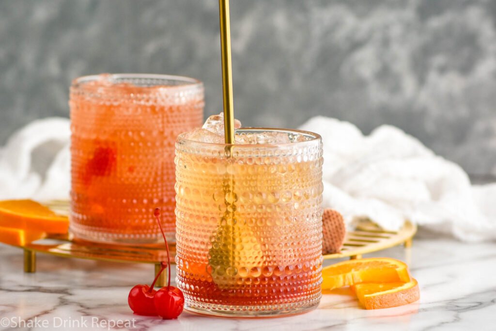 Side view of stirring stick in tumblers for Cherry Old Fashioned recipe. Orange slices and cherries beside.