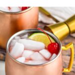 Pinterest graphic for Cherry Moscow Mule. Text says "the best Cherry Moscow Mule shakedrinkrepeat.com" Image shows a copper mug of Cherry Moscow Mule, ice, lime and cherry.