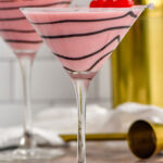 Side view of Chocolate Covered Cherry Martini with chocolate swirled on the glass and cherries as garnish. Cocktail jigger and cherries for garnish beside.