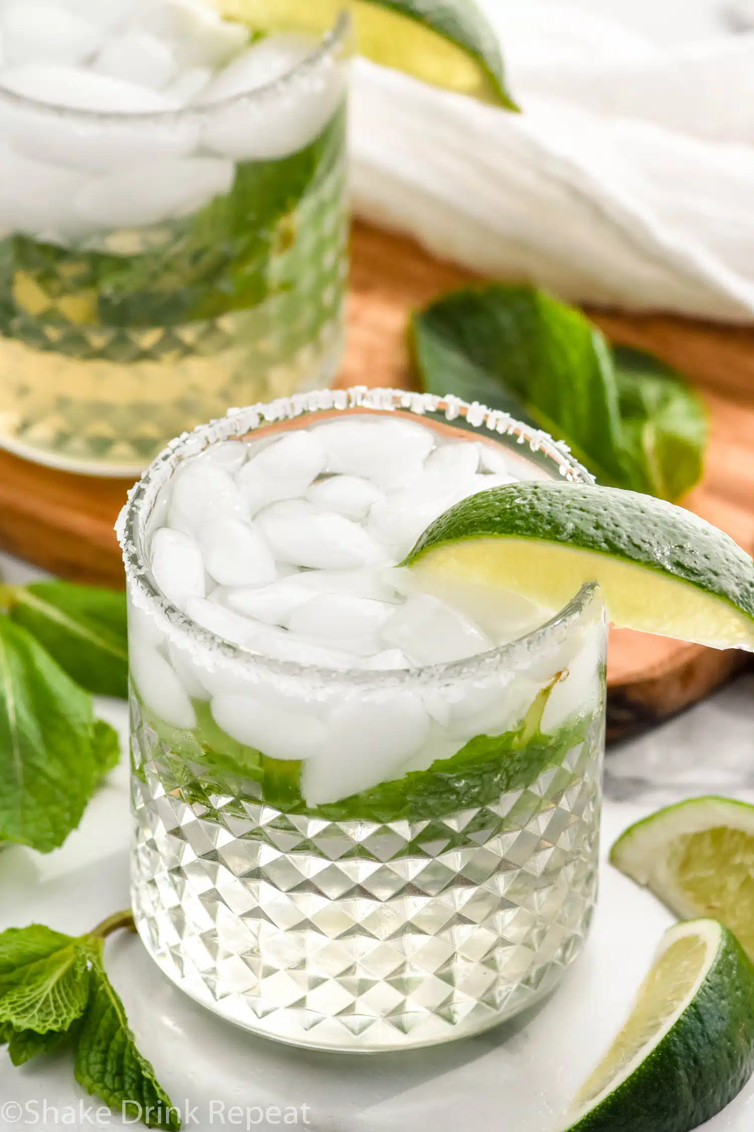 two glasses of Mojito Margarita with fresh mint leaves and lime wedges surrounding