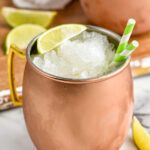 Moscow Mule Slush served in copper mug with straws and lime wedge. Additional lime wedges beside.