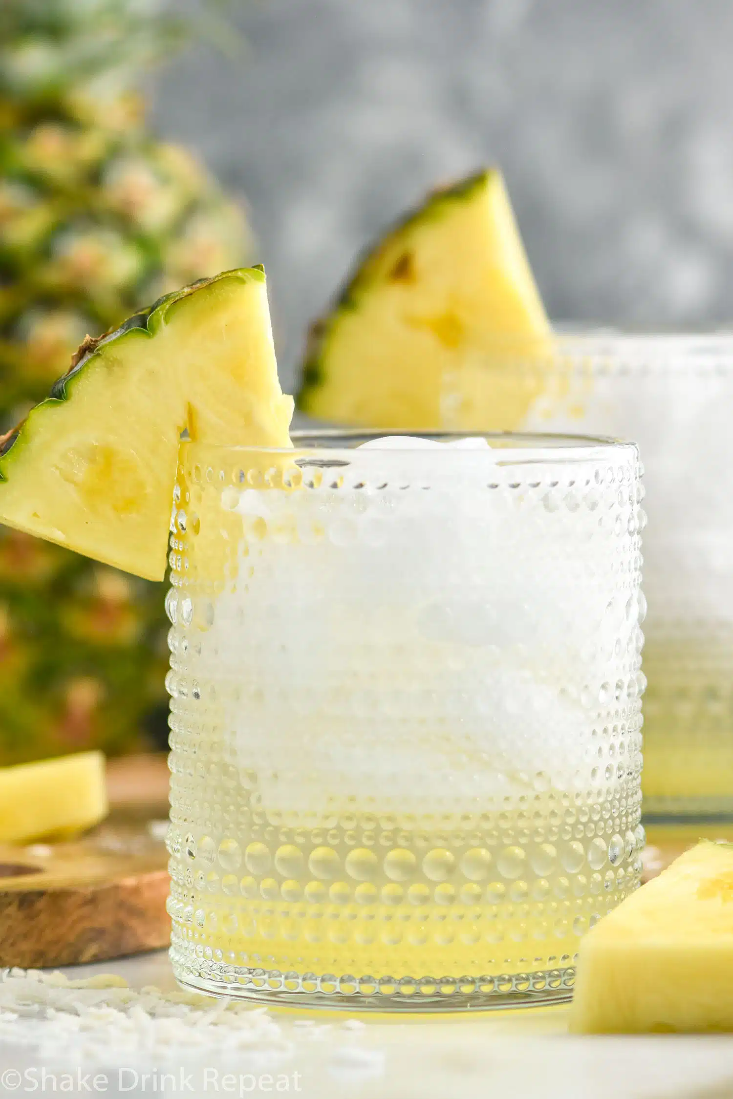 two glasses of Pina Colada Vodka Soda with ice and garnished with pineapple wedge. Fresh pineapple sitting in background.