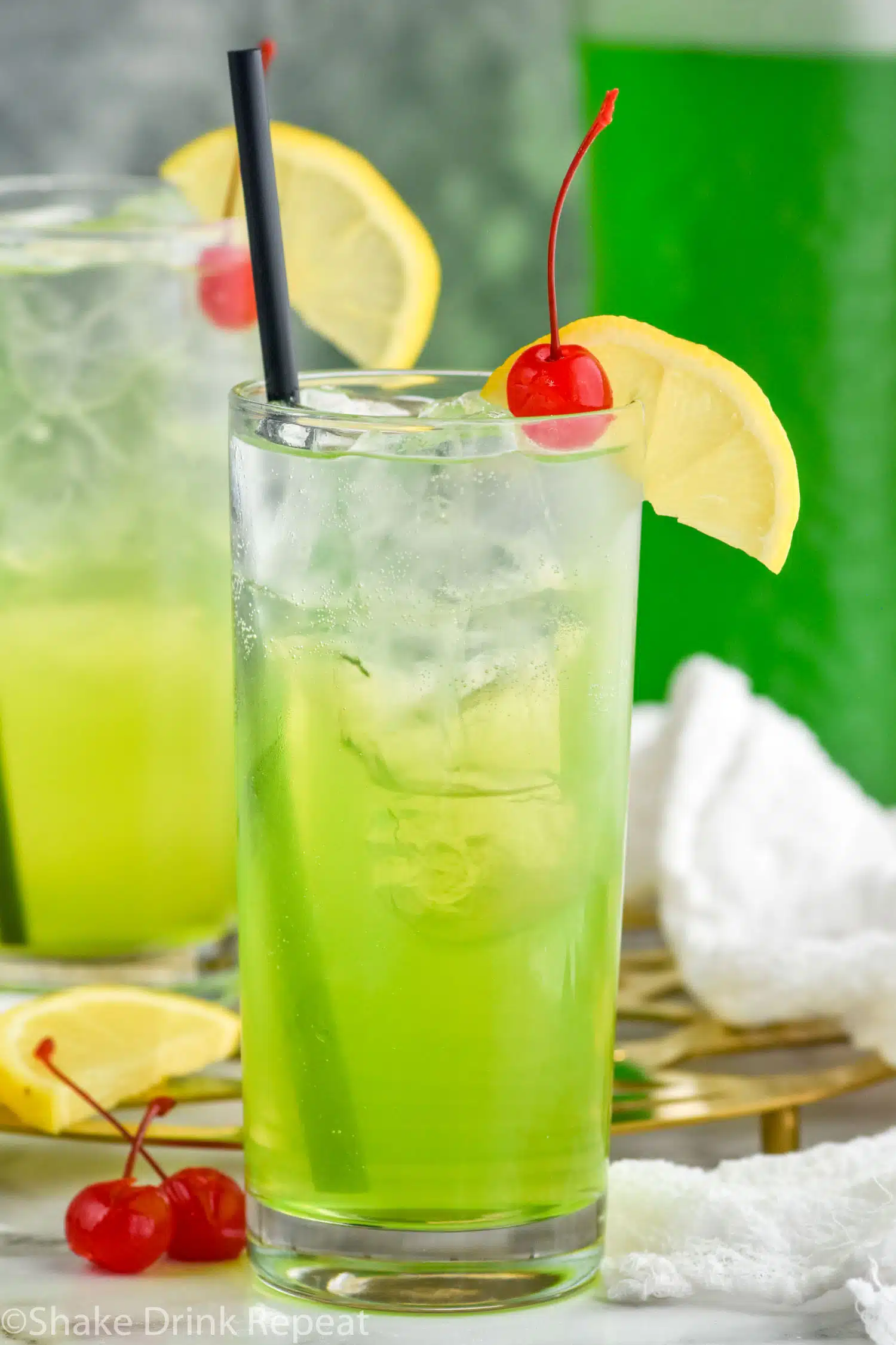 Two glasses of Tokyo Tea with ice, straw, lemon slice, and cherry